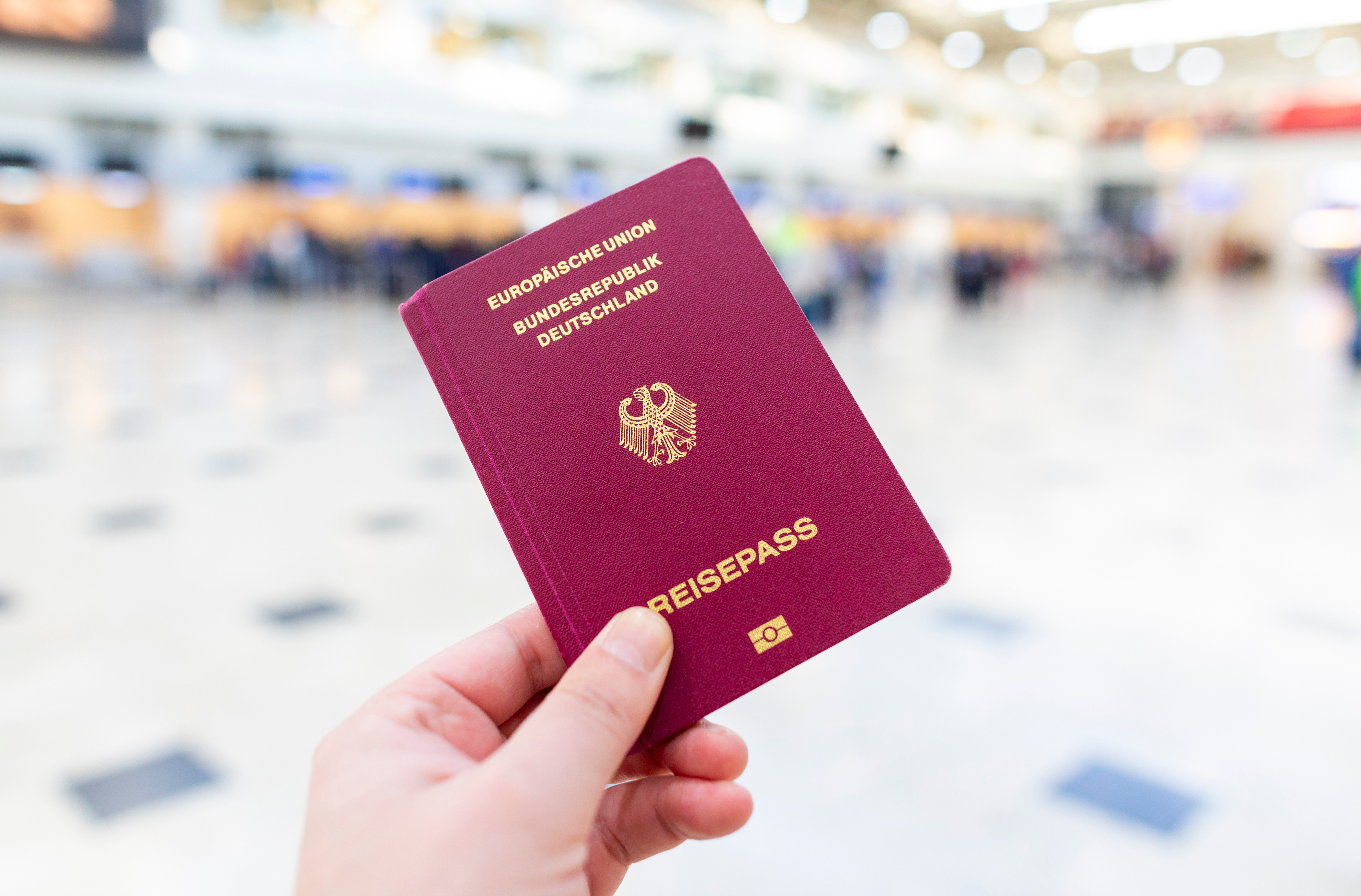 A hand holds a german passport in an airport terminal