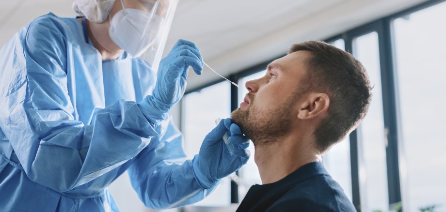 Medical Nurse in Safety Gloves and Mask, Protective Face Shield and Overalls is Taking a PCR Corona Virus Sample in a Health Clinic. Doctor Uses Respiratory Swab Test. Covid-19 Pandemic Concept.